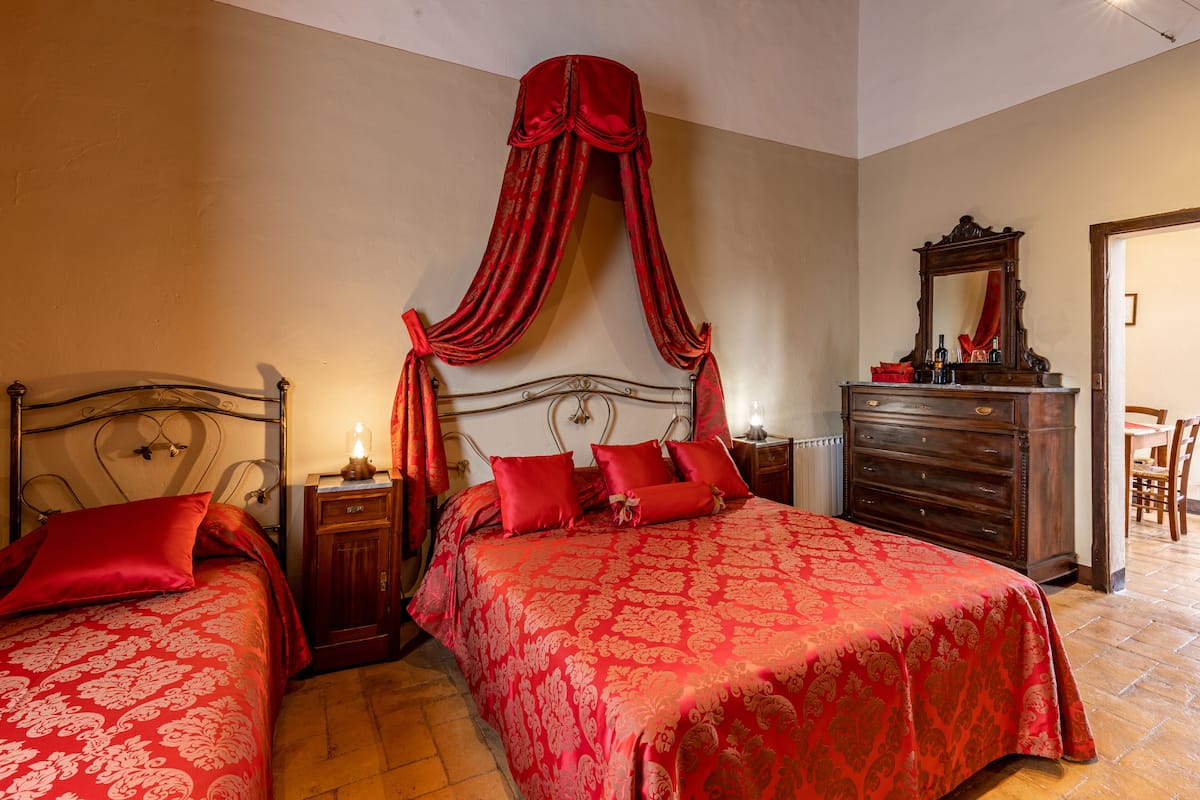 Une chambre avec deux lits, une commode en bois, un miroir et un lit à baldaquin rouge.