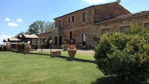A stone building with a courtyard, large potted plants, and a well-maintained lawn. - Wine Resort Colsereno (Montalcino)