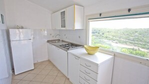 A kitchen with white cabinets, a gas stove, a sink, and a window with a view of greenery. - Appartamenti Casa Serena (Capoliveri)