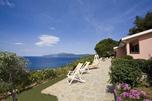 A stone pathway leading to lounge chairs overlooking a coastal view. - Appartamenti Casa Serena (Capoliveri)