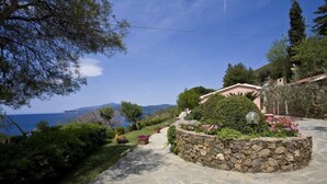 A stone pathway leading to a stone-walled garden with a view of the sea and mountains. - Appartamenti Casa Serena (Capoliveri)