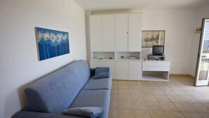 A compact living space with a sofa, kitchenette, and a television. - Appartamenti Casa Serena (Capoliveri)