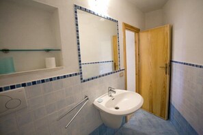 A bathroom with a white sink, a mirror, and a wooden door. - Appartamenti Casa Serena (Capoliveri)