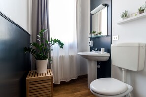 A bathroom with a white sink, toilet, and a potted plant on a wooden stool. - Castelmenardo39 (Treviso)
