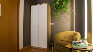 A room with a wooden floor, a white wardrobe, a yellow armchair, a small table with a book, and a hanging plant. - Castelmenardo39 (Treviso)