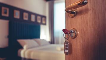 Habitación de hotel con puerta de madera, cama con ropa de cama blanca y cabecera con cuadros enmarcados.