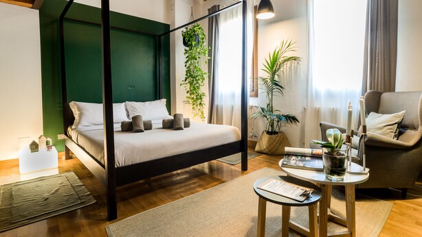 A modern bedroom with a four-poster bed, a sitting area with a table and chairs, and a large window providing natural light. - Castelmenardo39 (Treviso)
