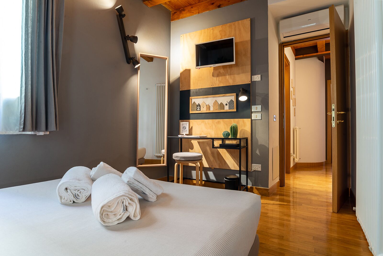 Una habitación de hotel con una cama grande, un escritorio con una silla, un espejo y un pequeño cactus sobre el escritorio.