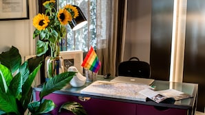 A desk with a laptop, a map, a rainbow flag, a sunflower vase, and a lamp. - Castelmenardo39 (Treviso)