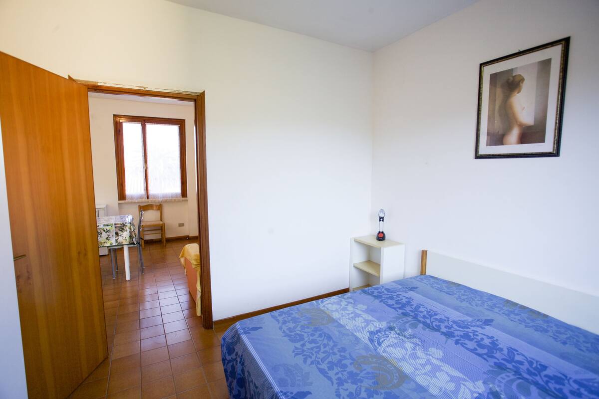 Une chambre à coucher avec un lit, une petite table de chevet, une chaise et une fenêtre.