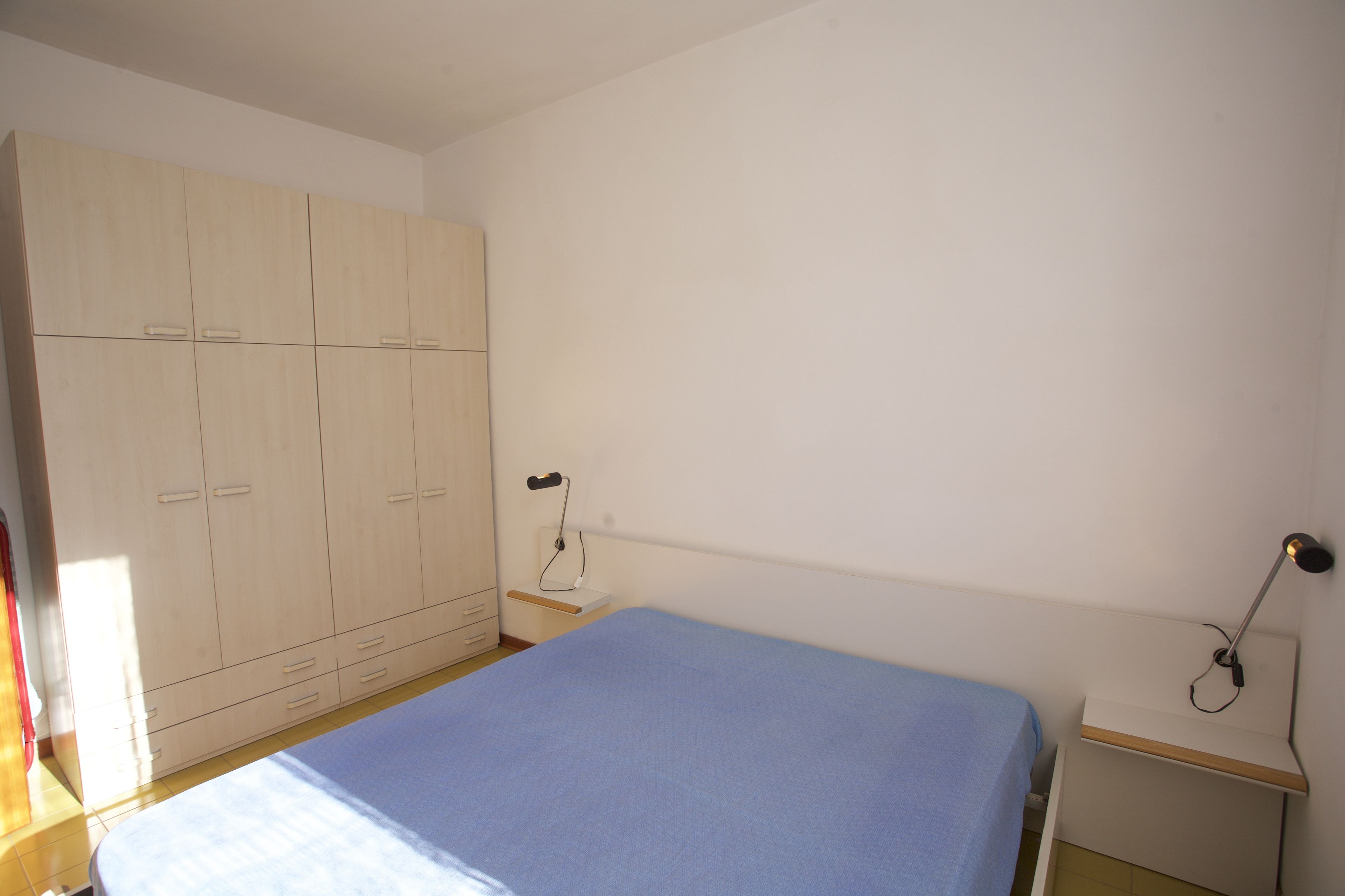 Une chambre à coucher avec un lit, une armoire, une table de chevet et une lampe.