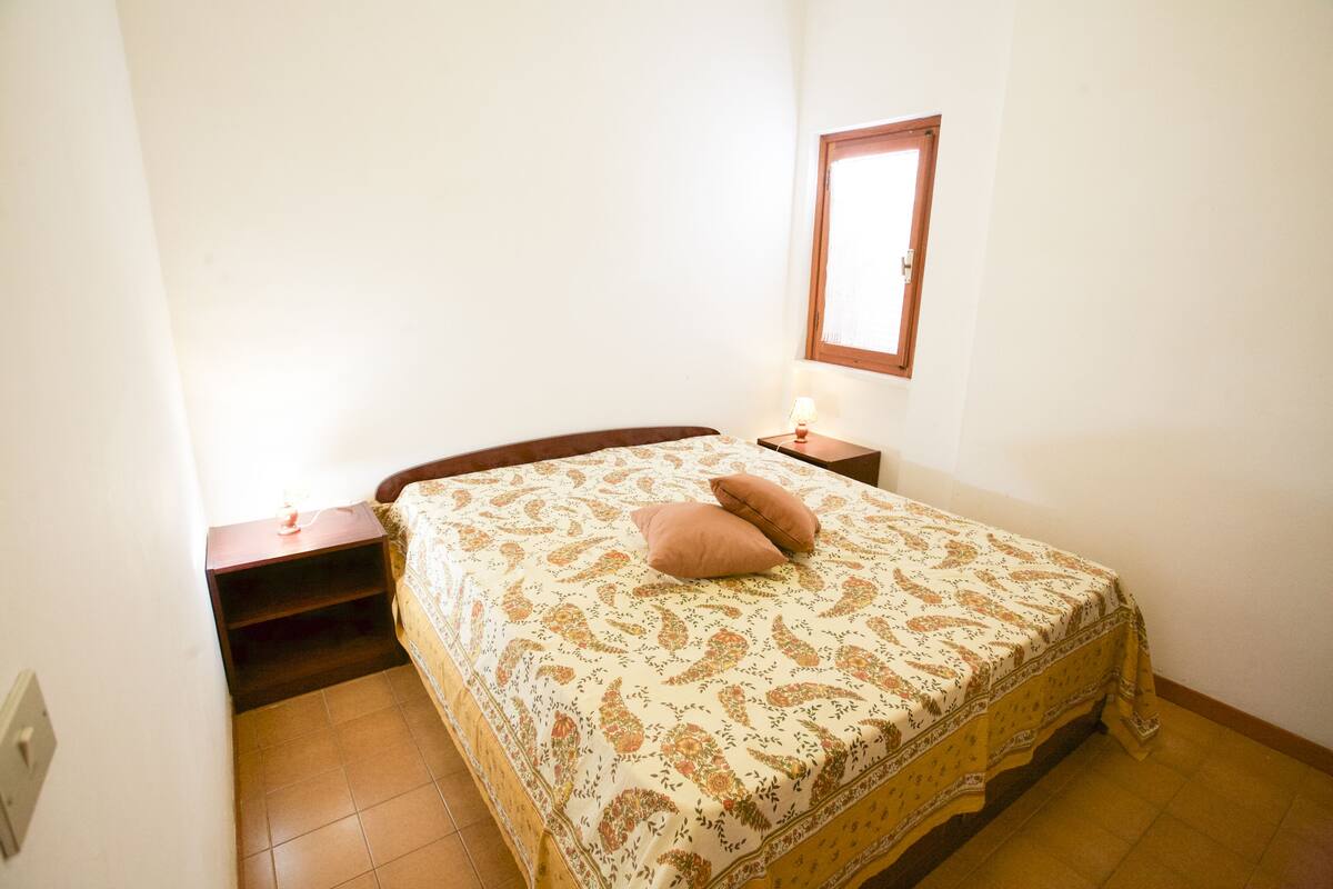 Une chambre à coucher avec un lit, une table de chevet, une lampe et une fenêtre.