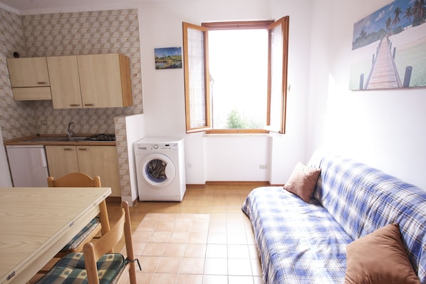 A compact kitchen with a washing machine, a dining table with chairs, and a sofa.