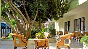 An outdoor patio with wicker furniture, a central table with a floral arrangement, and a building with large windows in the background.