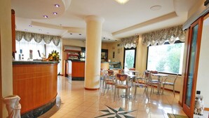 A hotel lobby with a reception desk, a bar area, and a seating area with chairs and tables.