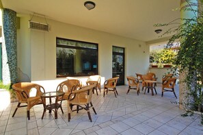 Un patio cubierto con muebles de mimbre, ventanas amplias y piso de baldosas.