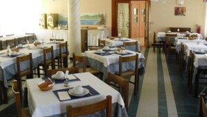 A dining area with multiple tables set for meals, wooden chairs, and a corridor leading to another room.