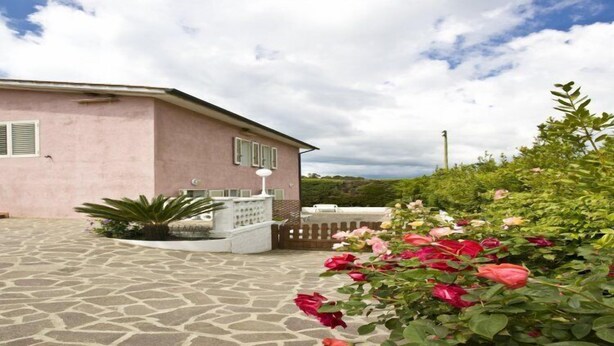 A pink building with a stone patio and a garden with roses. - Appartamenti Loredana (Capoliveri)