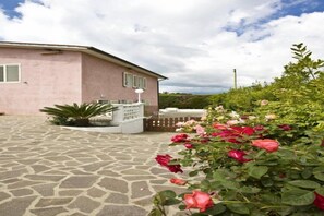 A pink building with a stone patio and a garden with roses. - Appartamenti Loredana (Capoliveri)
