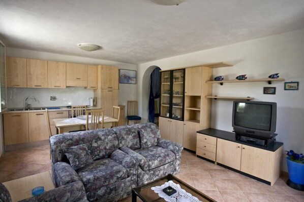 A compact living space with a sofa, a television, and a kitchen area. - Appartamenti Loredana (Capoliveri)