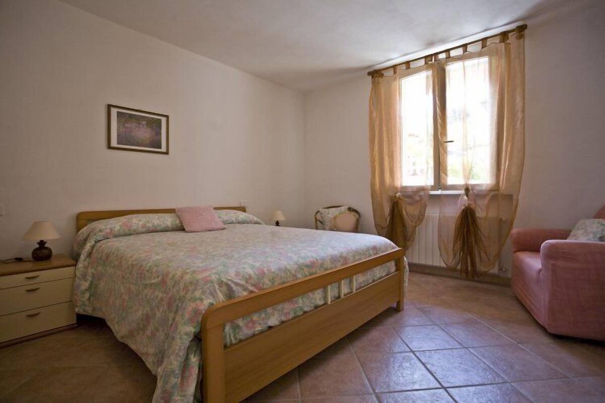 Een slaapkamer met een houten bed, een nachtkastje, een stoel en een raam met gordijnen.