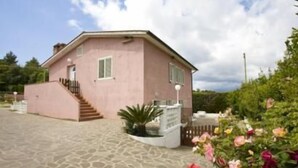 A pink house with a staircase leading to the entrance, a small garden, and a paved driveway. - Appartamenti Loredana (Capoliveri)