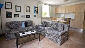A living room with a sofa and a coffee table, a kitchen with wooden cabinets, and a dining area with chairs. - Appartamenti Loredana (Capoliveri)