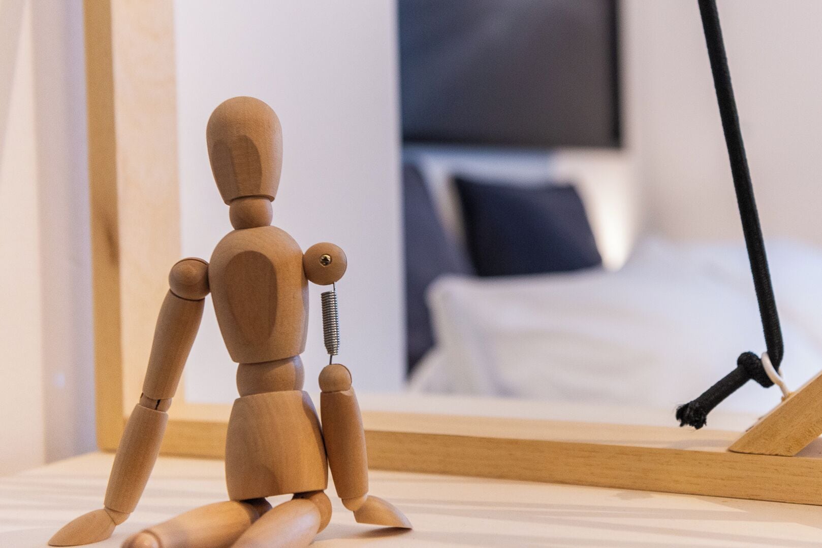 A wooden mannequin in a room with a bed and a black cable.
