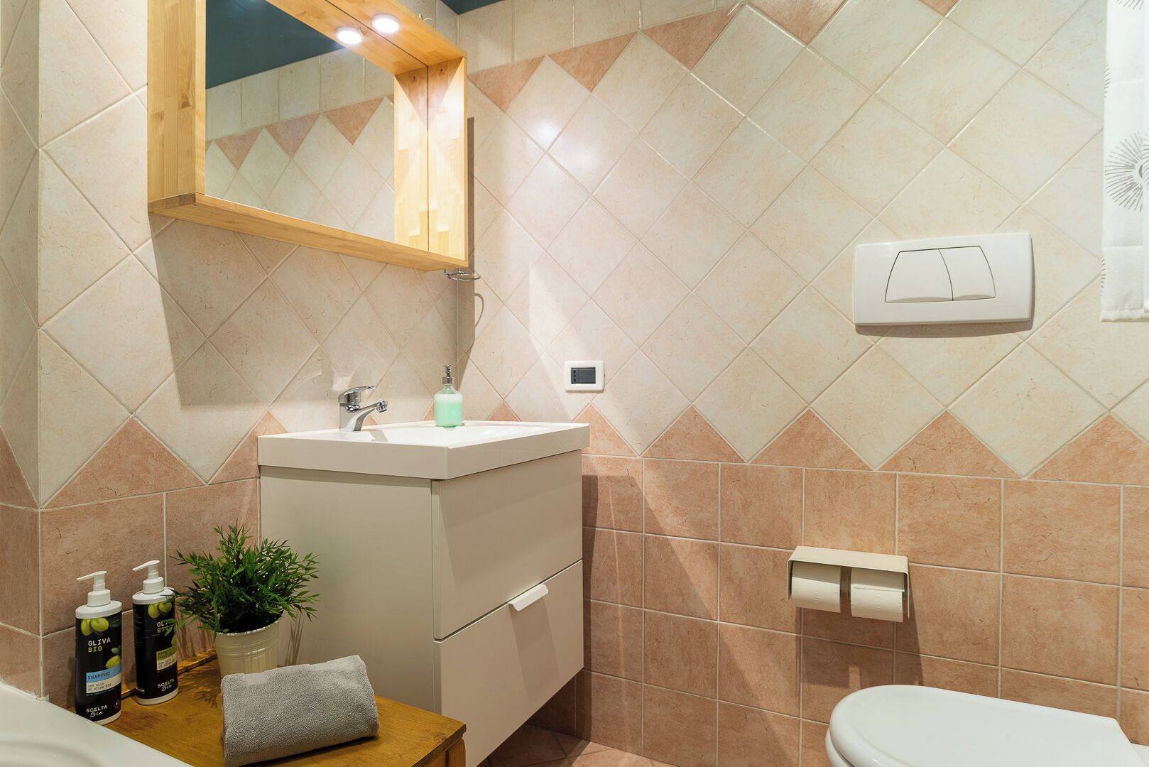 A bathroom with a sink, mirror, and toilet. There are toiletries on the counter and a towel on the floor.