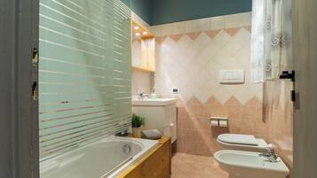 Un baño moderno con una bañera, un lavabo y un inodoro. Hay un mueble de tocador de madera, una planta en maceta y un perchero para toallas.