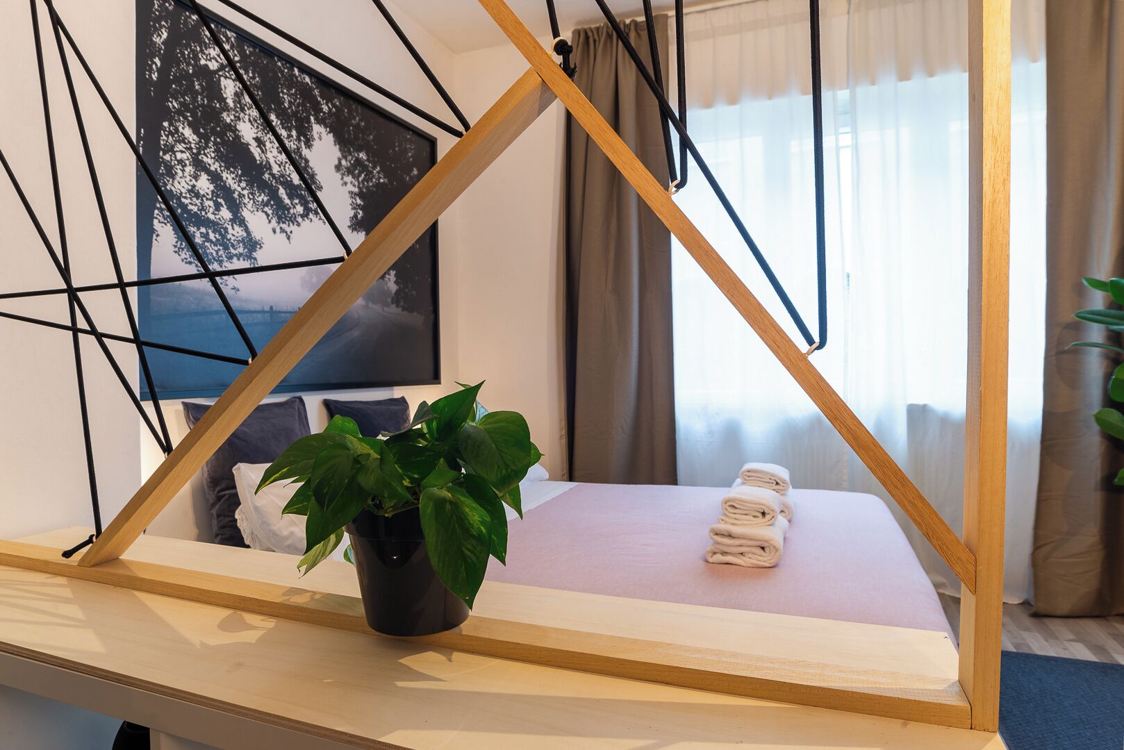 A modern room with a wooden-framed window, a potted plant, and neatly folded towels on a bed.
