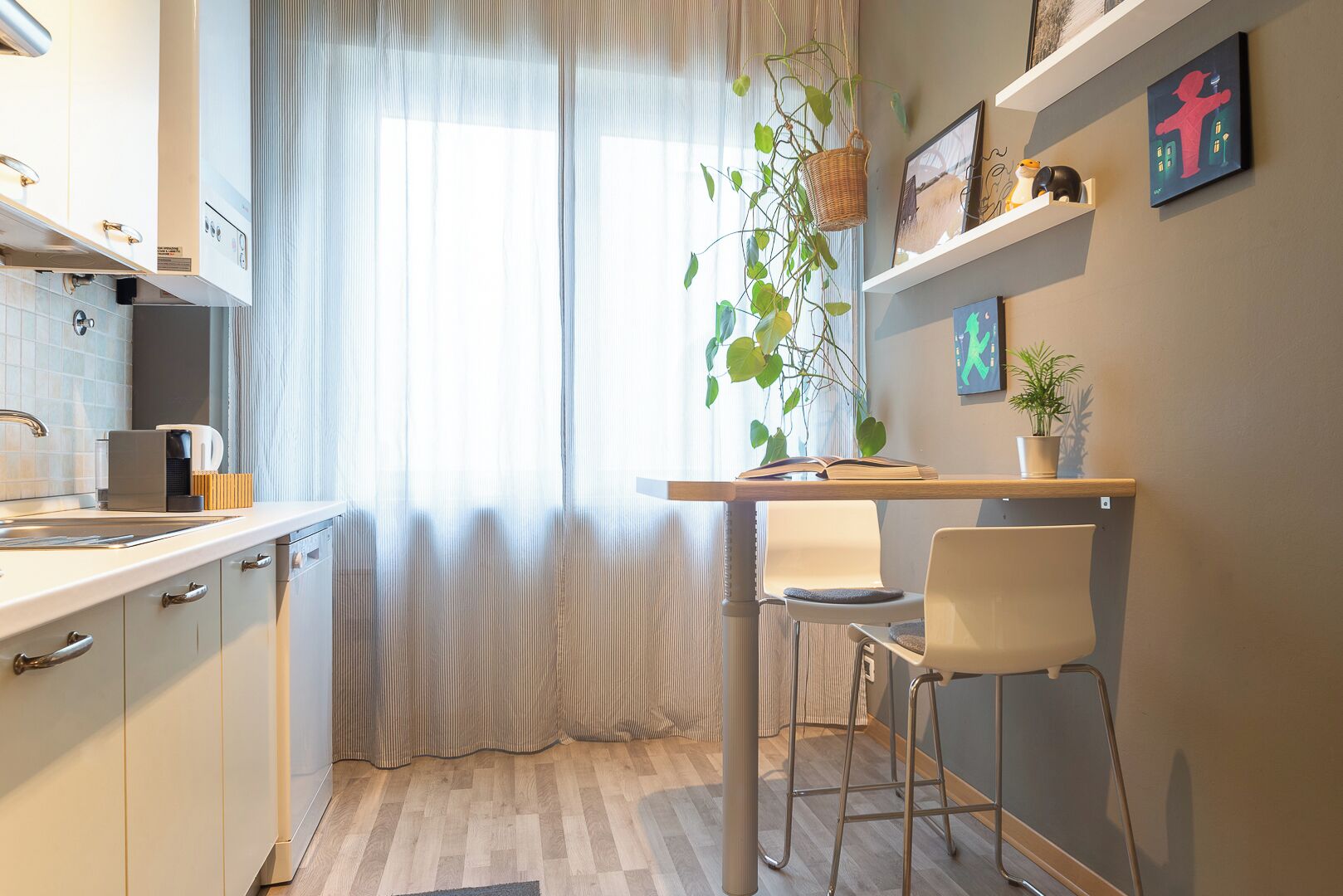 Una cocina moderna con encimera blanca, electrodomésticos de acero inoxidable y una ventana con cortinas traslúcidas.