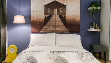 A bedroom with a bed, pillows, a bedside table with a lamp, a clock, and a wall-mounted shelf with a plant.