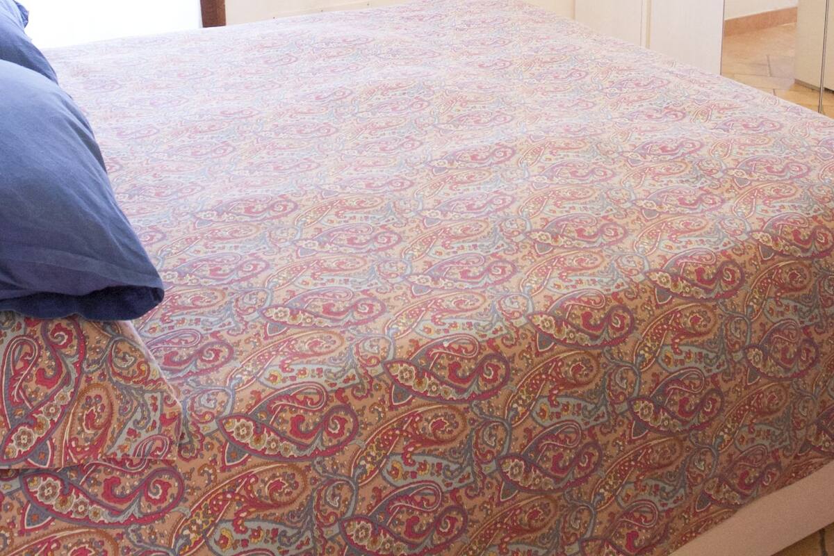 Ein Bett mit einem gemusterten Bettbezug und einem blauen Kopfkissen.