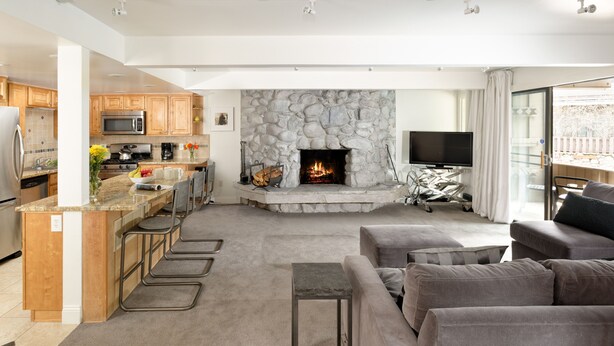 Eine moderne Küche mit Kamin aus Stein, einem Essbereich und einem Wohnzimmer mit Sofa und Fernseher.