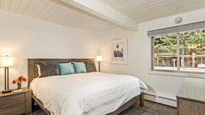 Ein Schlafzimmer mit Bett, Nachttischen, einem Fenster mit Blick und einem gerahmten Bild an der Wand.