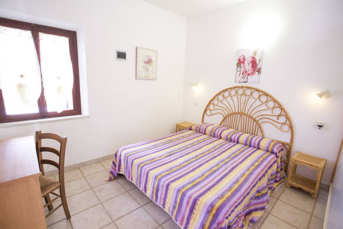 A bedroom with a bed, a chair, a small table, and a window.