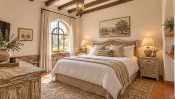 Un dormitorio con una cama grande, vigas de madera, pared de piedra, una ventana con cortinas y un cuadro en la pared.