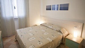 A bedroom with a bed, a nightstand, a drawer, and a window with curtains. There are three framed pictures on the wall. - Appartamenti Nisportino (Rio)