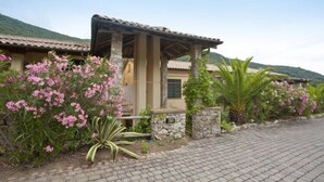 A building with a tiled roof, a stone wall, and pink flowering plants. - Appartamenti Nisportino (Rio)