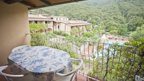 A balcony with a table and chairs, overlooking a lush green landscape with buildings and a pool. - Appartamenti Nisportino (Rio)