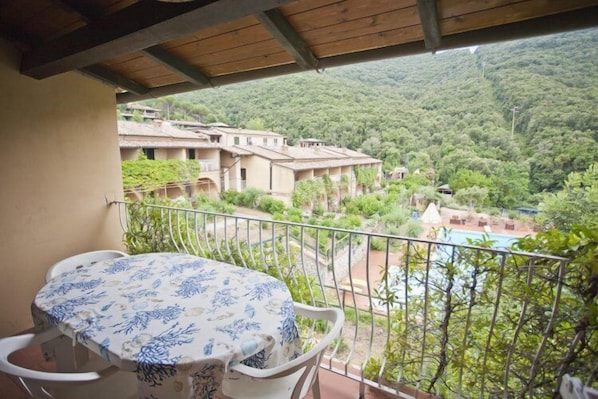 A balcony with a table and chairs, overlooking a lush green landscape with buildings and a pool.