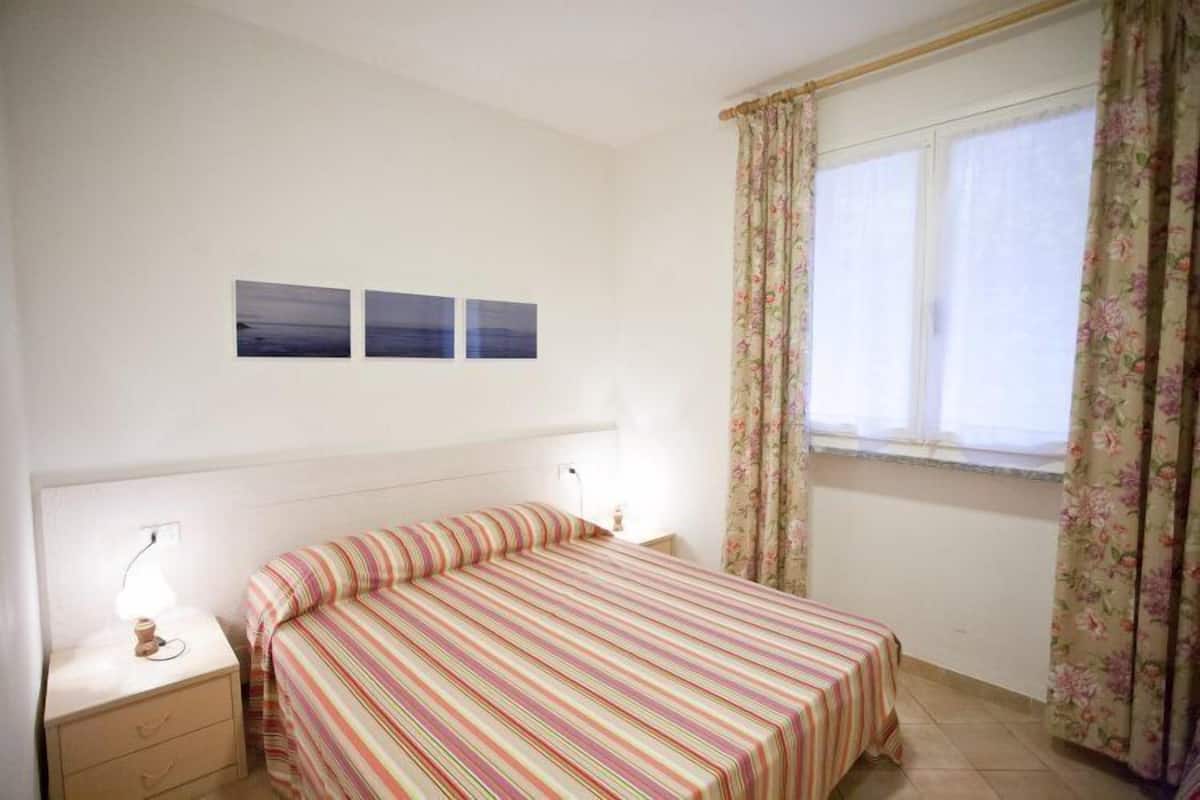 A bedroom with a bed, a nightstand, a lamp, and a window with floral curtains.
