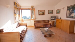 Una sala de estar acogedora con un sofá, una mesa de centro de vidrio, un televisor y una ventana con cortinas.