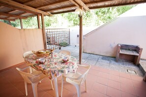 An outdoor patio with a table set for dining, surrounded by chairs, and a grill area. - Appartamenti Norsi (Capoliveri)