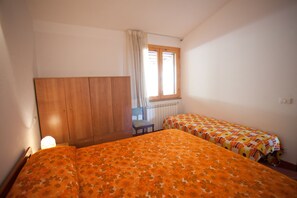 A bedroom with two beds, a wooden wardrobe, a chair, and a window with curtains. - Appartamenti Norsi (Capoliveri)