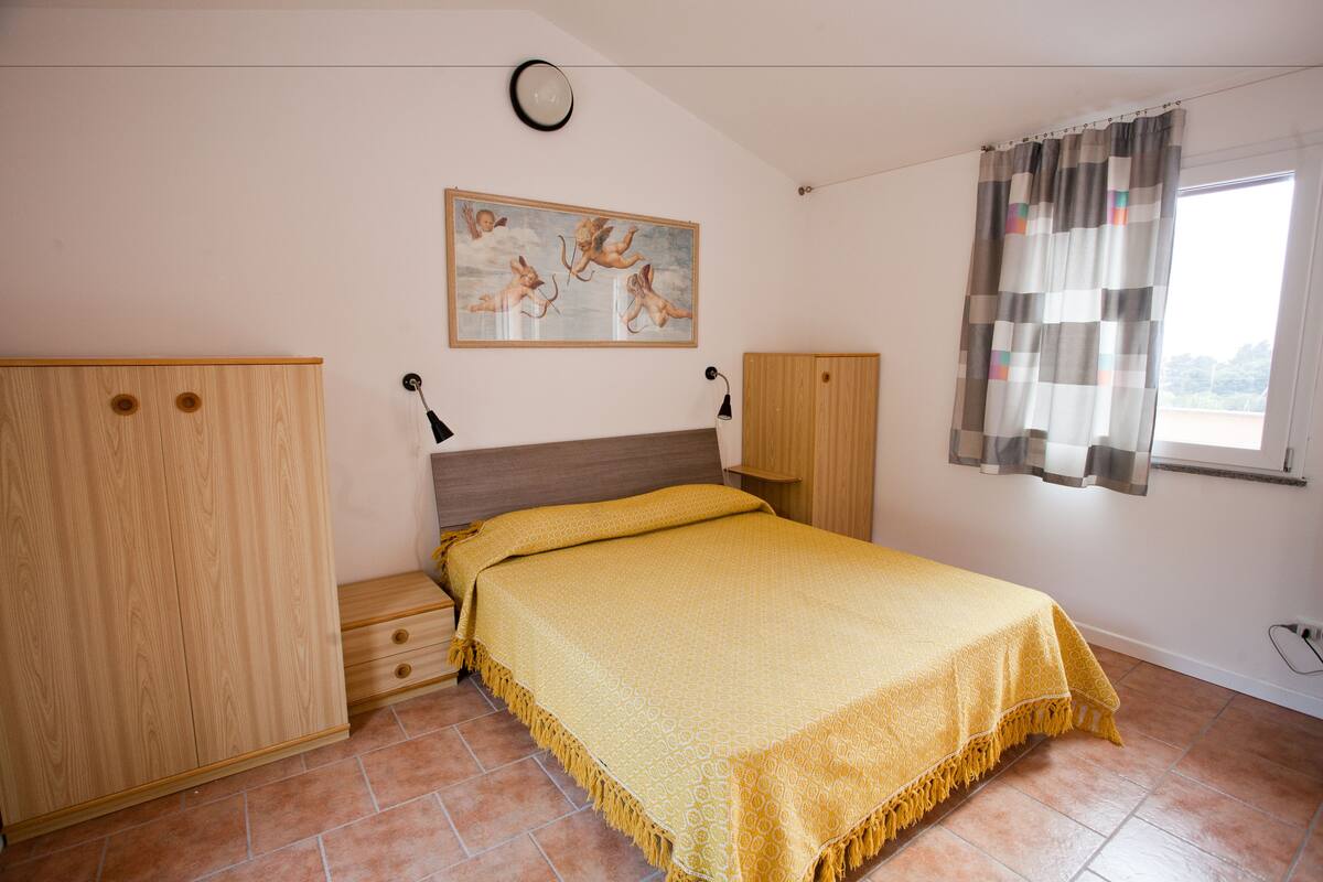 A bedroom with a bed, wooden wardrobe, and a painting on the wall.