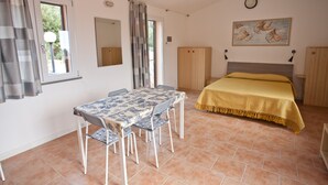 Un dormitorio con cama, una mesa con sillas, una ventana con cortinas, un espejo y un cuadro en la pared.