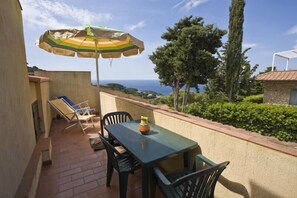 Una terraza con mesa y sillas, un parasol a rayas y vista al mar.