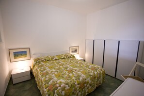 A bedroom with a floral bedspread, a bedside table with a lamp, a framed picture on the wall, and a wardrobe. - Appartamenti Serena (Capoliveri)